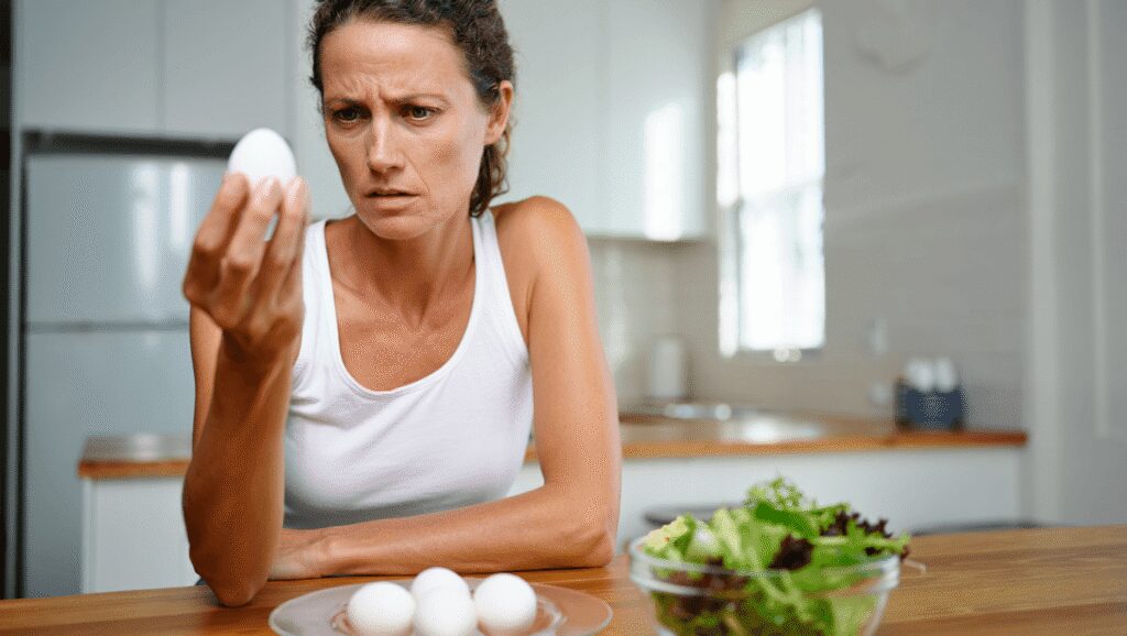 Woman refusing to eat eggs. Egg Free Affected Allergy Banned Restriction. Young beautiful woman holding fresh egg at home with open hand doing stop sign with serious and confident expression