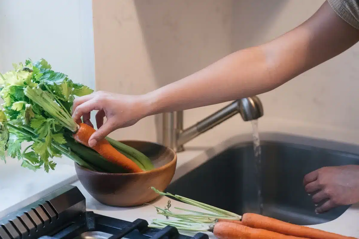 Mains lavant des légumes frais sous l'eau courante dans un évier de cuisine