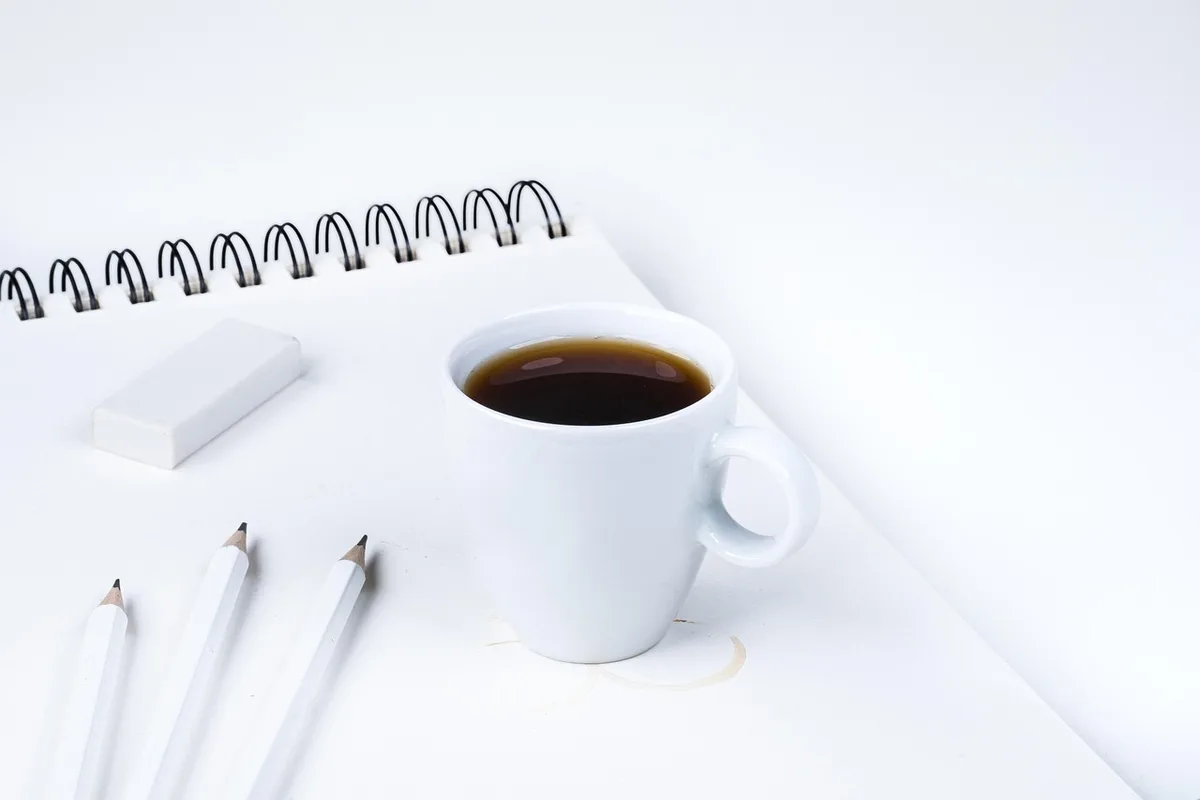 Mains tenant des tasses près d'un carnet sur une table de café en plein jour