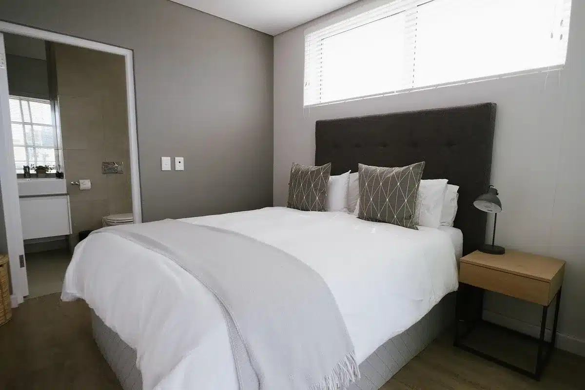 Chambre claire en journée avec lit, table de chevet et rideau laissant passer la lumière